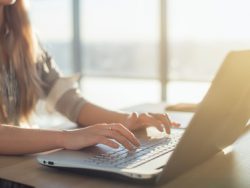 Female writer typing using laptop keyboard at her workplace in the morning. Woman writing blogs online, side view close-up picture